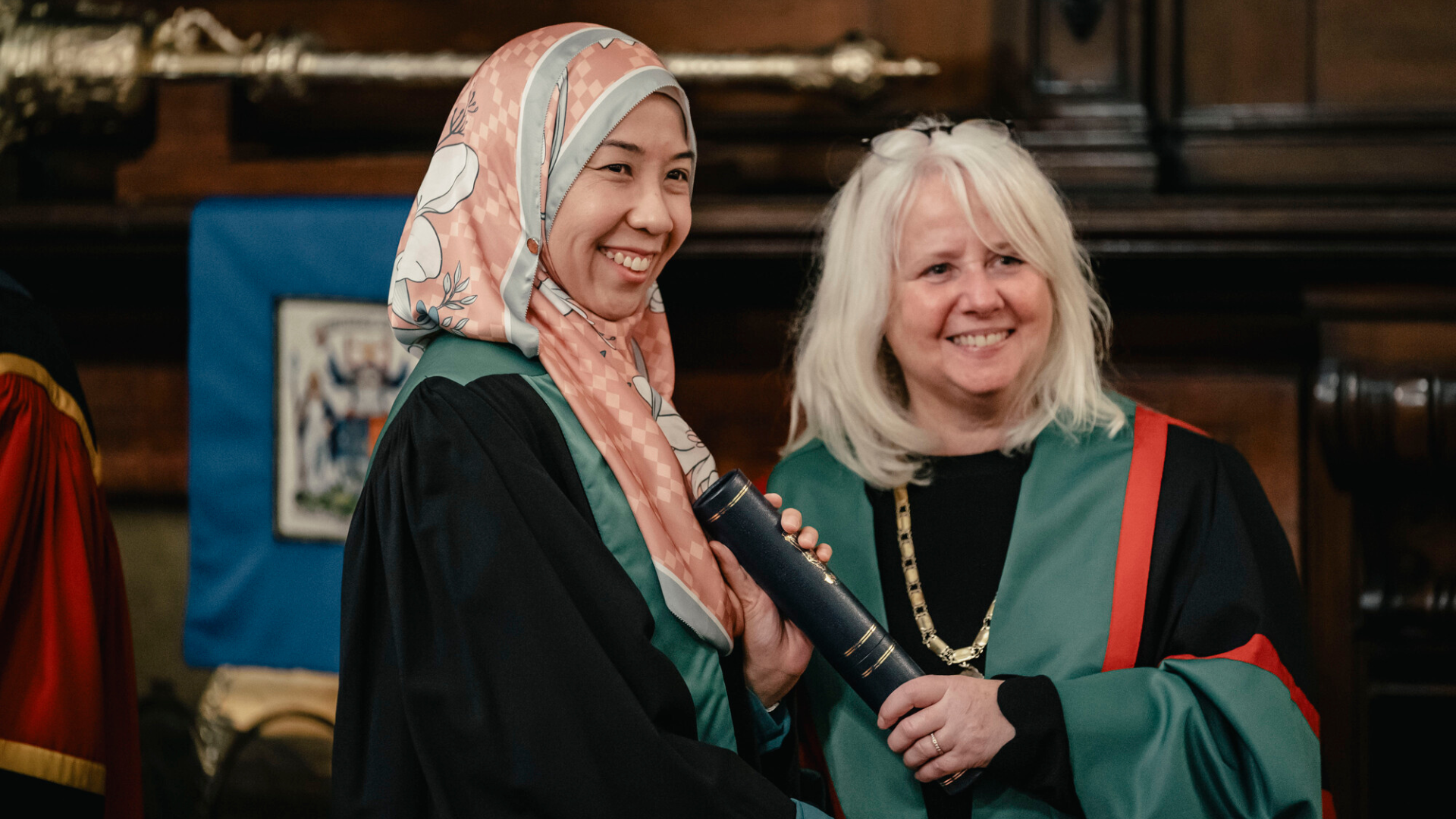 A woman wearing a patterned headscarf is handed her diploma